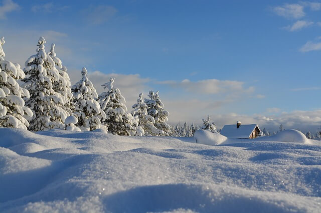 Tiefverschneite Berglandlandschaft. Blauer Himmel. Schnee klitzert in der Sonne. Rechts sind Berghütten im Schnee zu erkennen.